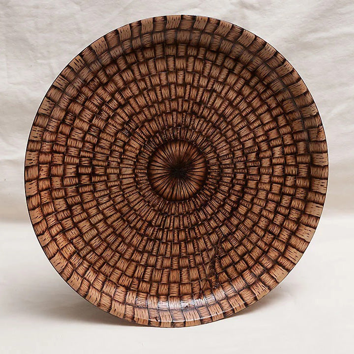 A wooden platter with a woodburned geometric pattern radiating out from the center. 