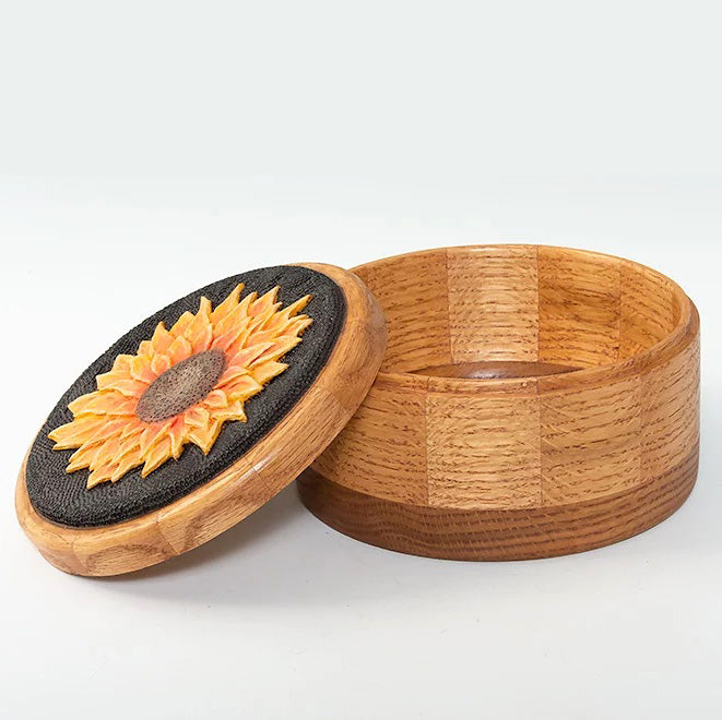 A woodturned lidded bowl with a sunflower burned and carved on the lid. The lid is black and yellow in color. 