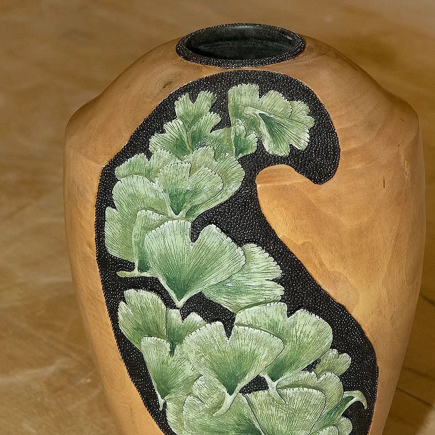 A woodturned vase with ginko leaves carved and painted on the side, painted green. 