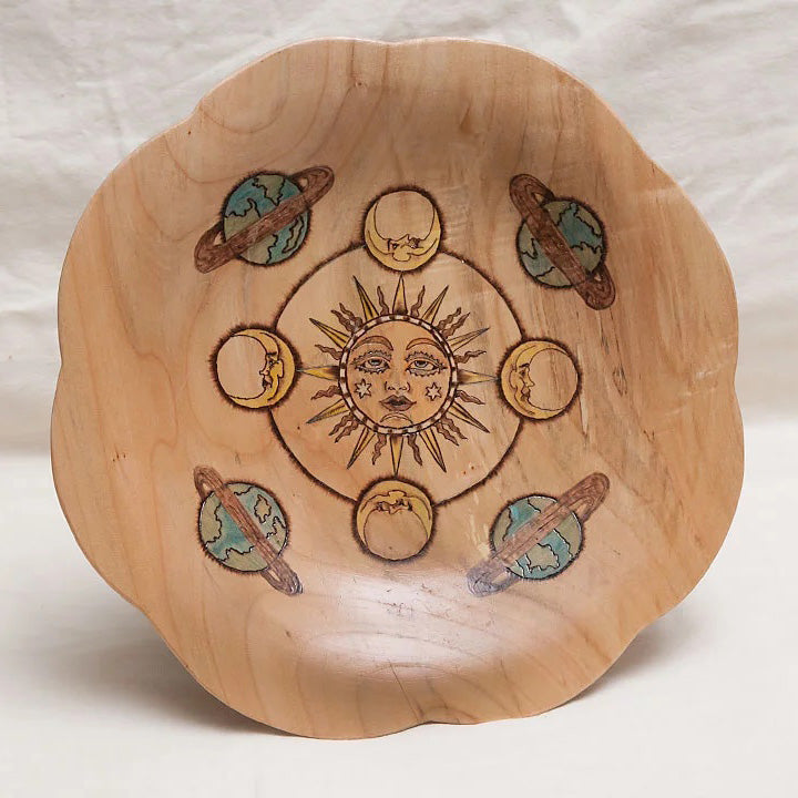 A curved-edge platter with a sun, moons and planets burned and painted on it. 