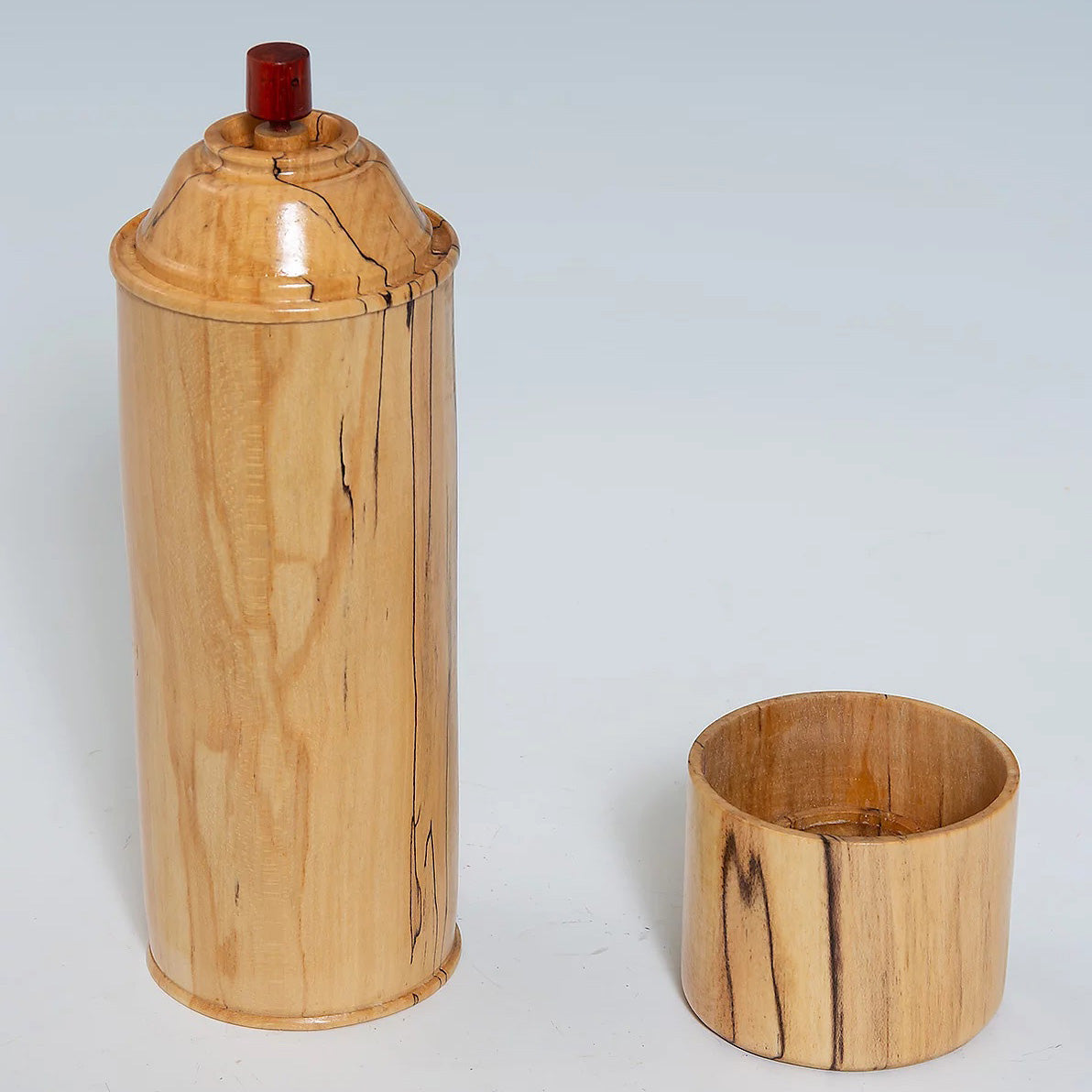 A wooden replica of a spray paint can with the lid off. The wood is light colored. 